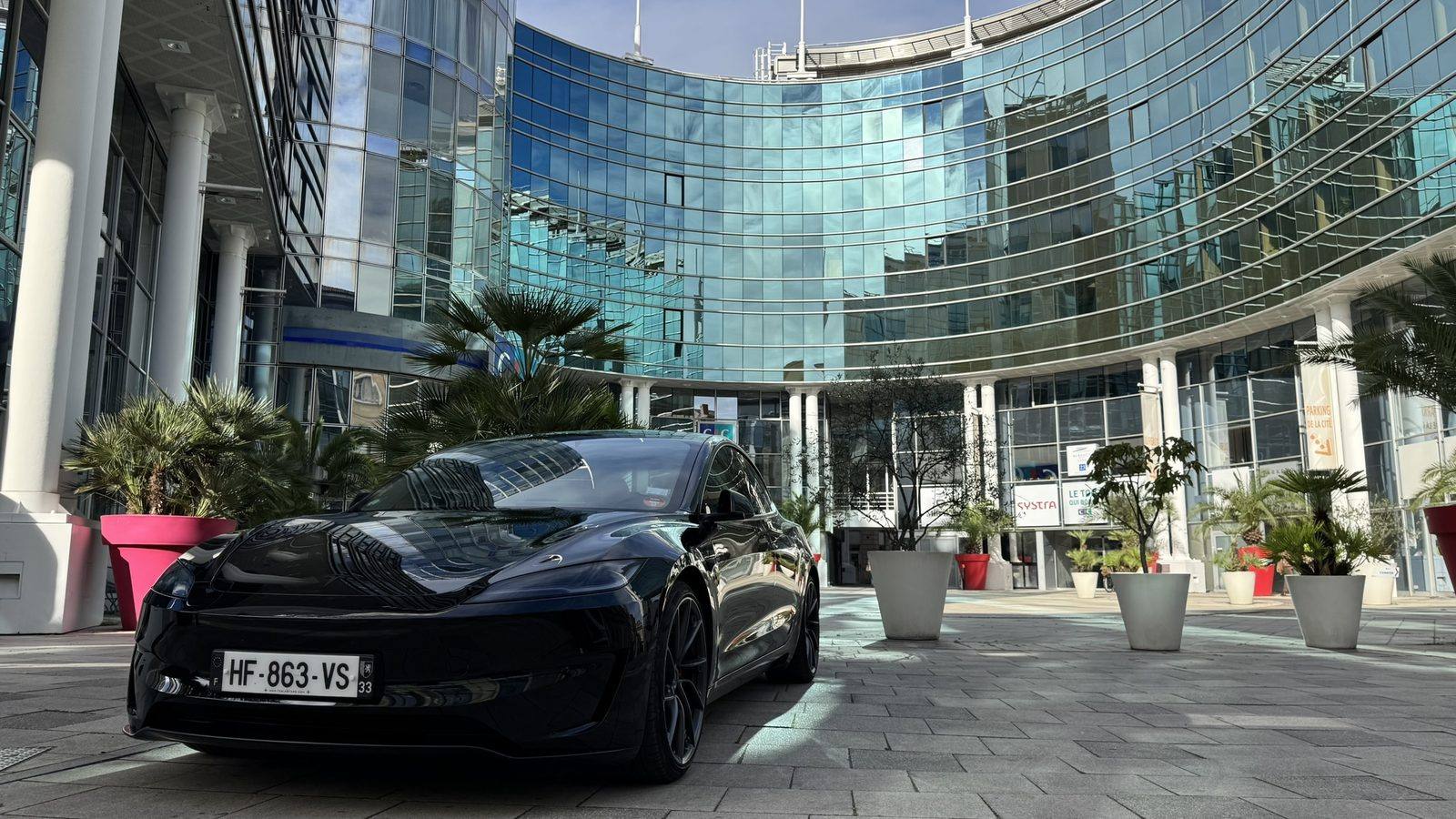 Tesla Model 3 noire devant la façade vitrée de la Cité Mondiale, Bordeaux